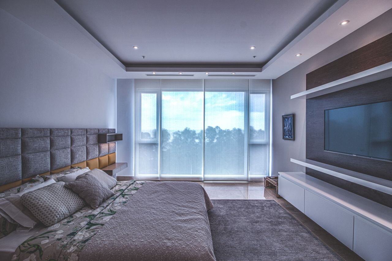 Services Spacious luxury bedroom with a modern design, featuring a large window and a wall-mounted TV.