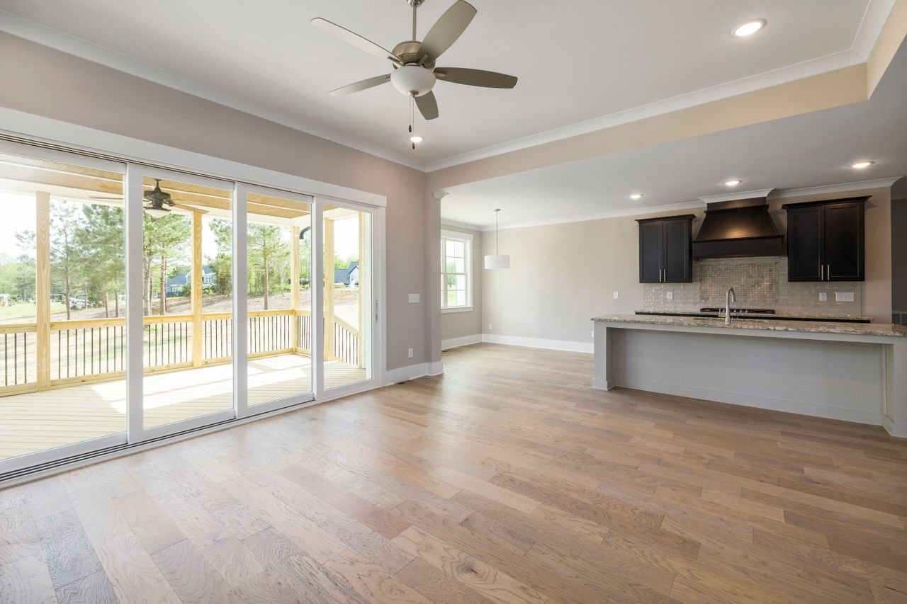 Bright open-plan interior with wooden flooring and large glass doors leading to a veranda.